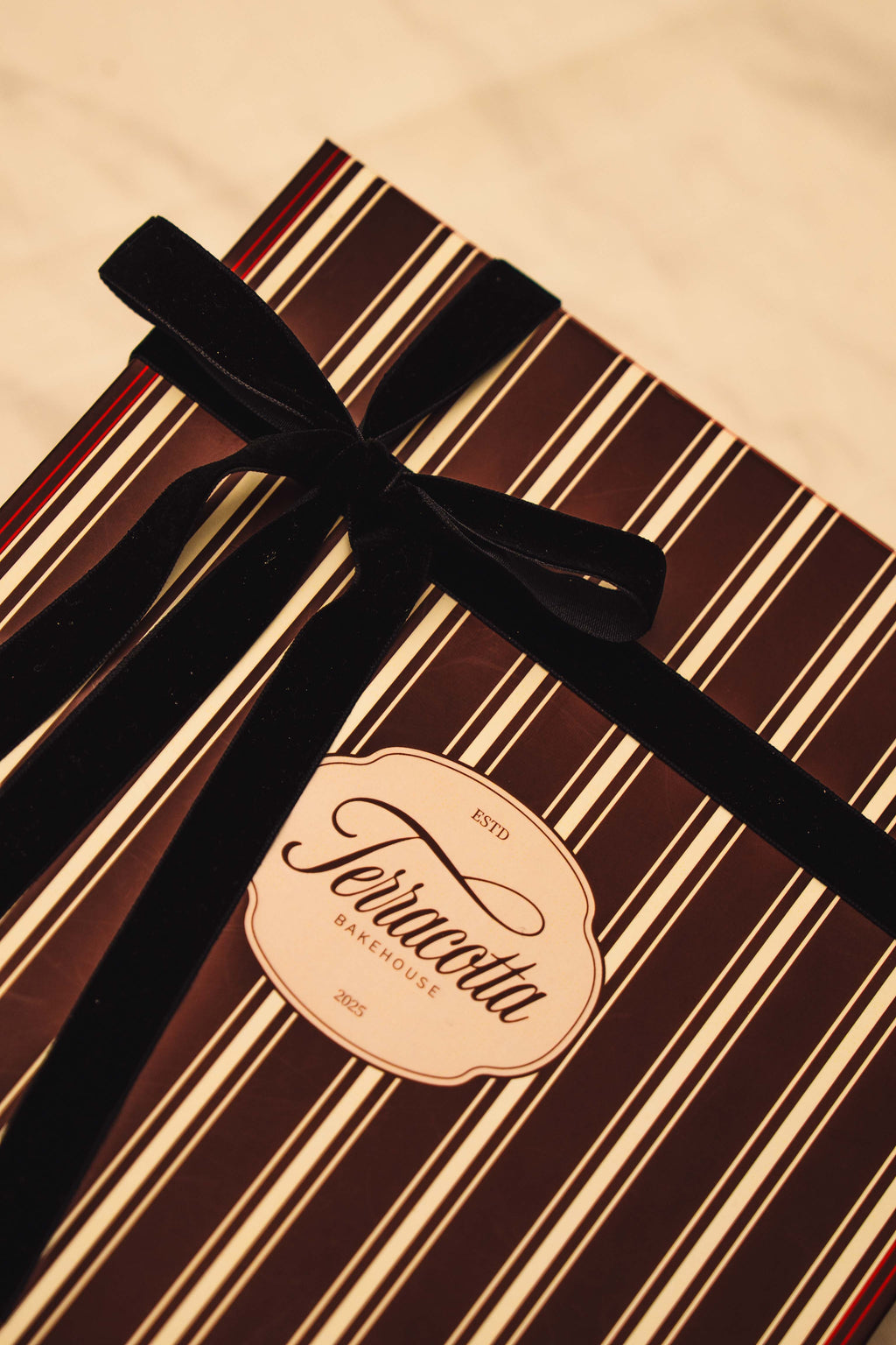 Gift box with striped pattern and black ribbon, featuring a label on a beige background